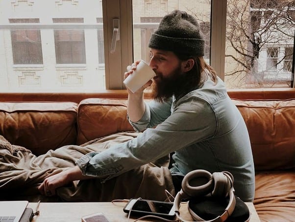 A bearded man wearing a beanie drinks from a white paper cup and smiles as he does so because he now knows the answer to the question: what is tenant insurance?